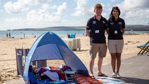 Two face to face (F2F) fundraisers at the beach stood next to a tent filled with RNLI collateral