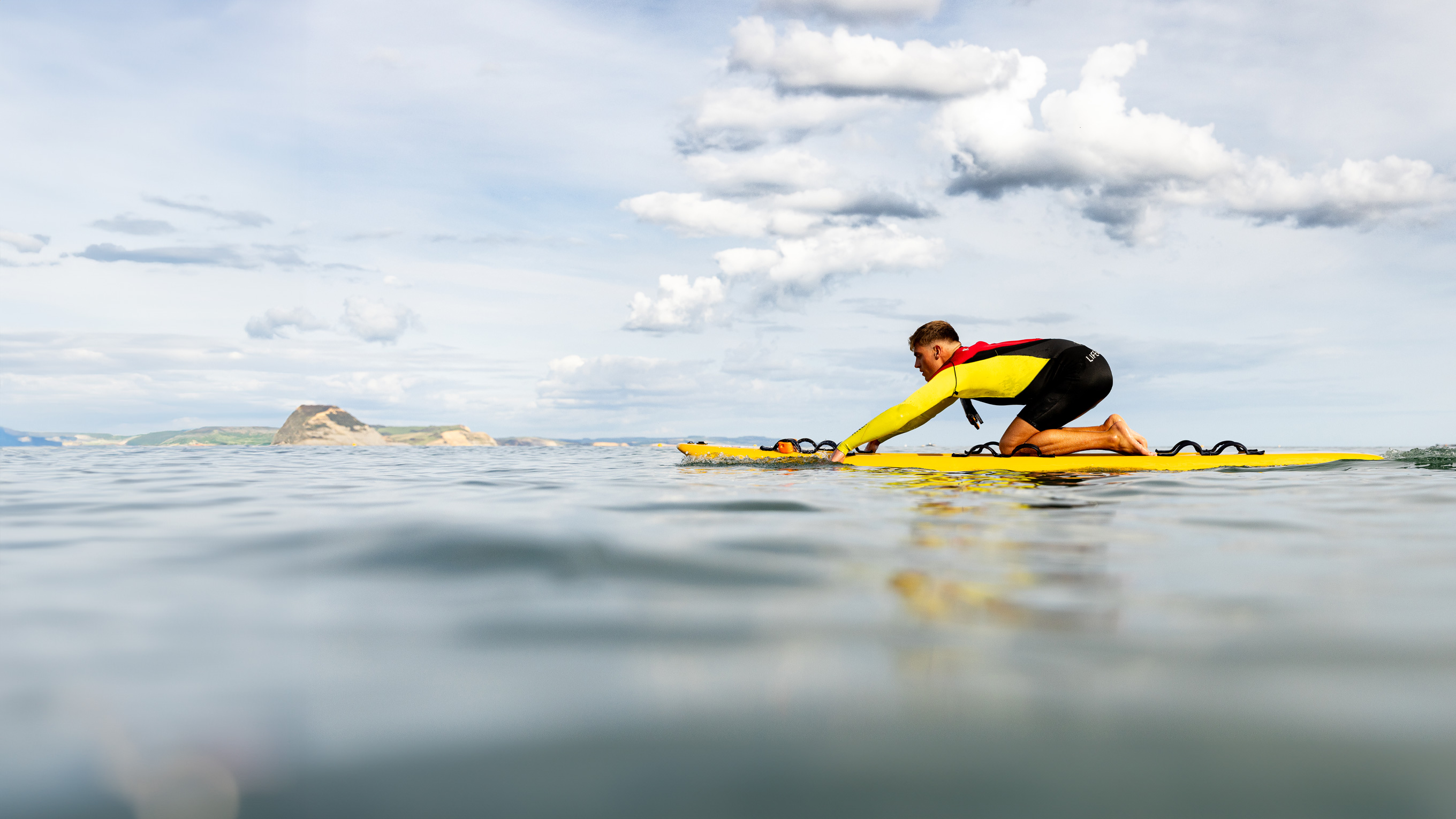 Ben Greenslade, West Dorset Lifeguard, patrolling Lyme Regis Beach using a rescue board.